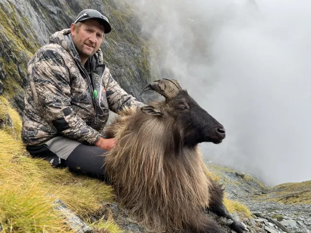 man with goat with mist of waterfall behind